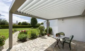 Un angolo relax sotto una vite a pergola semplice, con un tavolino e sedie, affacciato su un giardino fiorito.