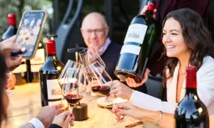 Brindisi con vino rosso, una bottiglia da 12 litri nome in mano, mentre si scatta una foto con lo smartphone.