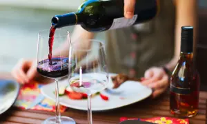 Versando vino rosso in un bicchiere, pronto per un perfetto abbinamento cibo vino con un piatto di carne e verdure.