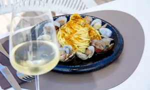 Un bicchiere di vino bianco, perfetto vino bianco da abbinare al pesce, accanto a un piatto di spaghetti alle vongole.