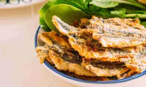 Piatto di alici fritte dorate e croccanti, servite con foglie verdi fresche.
