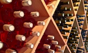Scaffale in legno con bottiglie di vino rosse e scure, disposte con la corretta inclinazione per la conservazione.