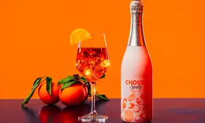 Un bicchiere di spritz ricetta perfetta, con ghiaccio e arancia, accanto a una bottiglia e arance fresche.