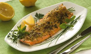 Filetto di trota salmonata cotto al forno con erbe aromatiche e limone, servito su un piatto bianco con guarnizioni fresche.