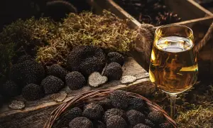 Truffles in a basket and on a wooden board, with a glass of white wine. La domanda è: che vino abbinare al tartufo?
