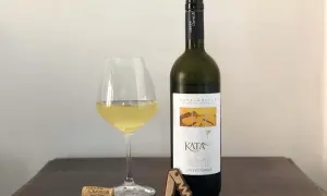 Un bicchiere di vino bianco e una bottiglia di Catalanesca del Vesuvio, con tappo e cavatappi sul tavolo.