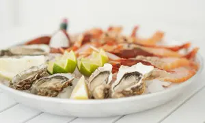 Piatto di ostriche fresche e gamberi, guarnito con spicchi di limone e lime. Un delizioso pesce bianco pronto da gustare.