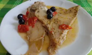 Piatto di pesce razza in umido con pomodorini e olive nere, condito con erbe aromatiche.