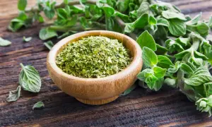 Un ciotola di legno piena di origano secco, con rametti freschi sullo sfondo. Il profumo di origano inebria l'aria.