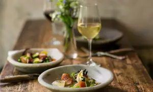 Un bicchiere di vino bianco per cucinare accompagna un pasto raffinato con piatti di pesce e verdure su un tavolo di legno rustico.
