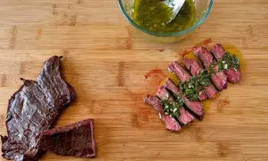 Fetta di manzo che carne è, succulenta e affettata, condita con salsa verde su tagliere di legno.