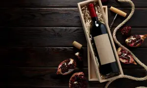 Una bottiglia di vino rosso in una scatola di legno, circondata da melograni e corda. Un assaggio dei **vini campani** più pregiati.