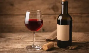 Un bicchiere di vino rosso, una bottiglia con etichetta vuota e un tappo vino su un tavolo di legno rustico.