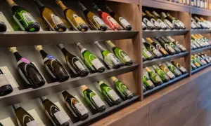 Scaffali pieni di bottiglie di champagne, alcune con etichette dorate e verdi. Una bottiglia da 5 litri nome è visibile in primo piano.