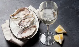 Un piatto di ostriche fresche su ghiaccio, accompagnato da un bicchiere di vino bianco frizzante e spicchi di limone. Un'elegante degustazione di ostriche e vino.