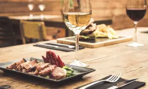 Un bicchiere di vino bianco, perfetto vino bianco per carne alla brace, accanto a un piatto di carne affettata e fragole su un tavolo di legno.