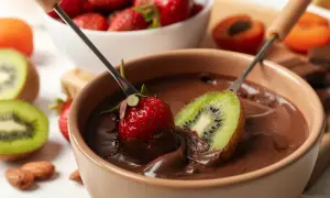 Fragole e kiwi immersi in una fonduta di cioccolato, un delizioso esempio di abbinamenti cioccolato e frutta.