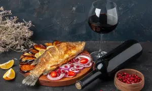 Un gustoso pesce fritto con melanzane, limone e cipolla, accompagnato da un bicchiere e una bottiglia di vino rosso da abbinare al pesce.