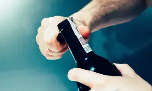 Mani che aprono una bottiglia di vino, rimuovendo la capsula.