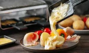 Formaggio fuso che cola su patate e salumi, un delizioso esempio di diversi tipi di formaggio usati per la raclette.