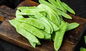 Un mucchio di taccole fresche, verdi e piatte, su un tagliere di legno scuro. Cosa sono? Deliziose!