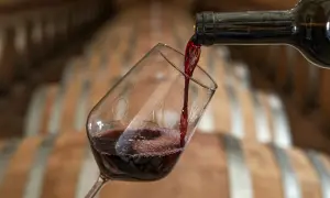 Versando vino rosso in un bicchiere, con botti di legno sullo sfondo. Attenzione, il vino contiene nichel.