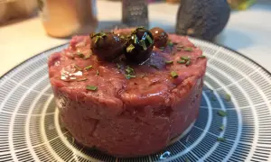 Un delizioso tartare di carne cruda, guarnito con olive nere e erba cipollina, pronto per essere gustato.