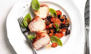 Tranci di rana pescatrice avvolti nel prosciutto, serviti con ratatouille di verdure e basilico fresco.