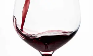Vino rosso porpora versato in un calice, creando un vortice invitante.