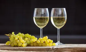 Due calici di vino bianco, tra i migliori vini bianchi italiani, accanto a un grappolo d'uva su un tavolo di legno.