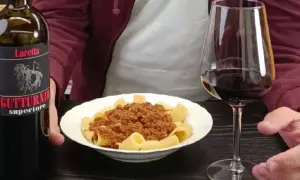 Un bicchiere di vino rosso e un piatto di pasta al ragù, accompagnati da una bottiglia di Gutturnio.
