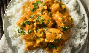 Piatto di riso bianco con pollo al curry arancione, guarnito con prezzemolo fresco. Perfetto con vino bianco o rosso.