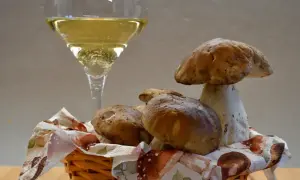 Un bicchiere di vino bianco frizzante, perfetto vino da abbinare ai funghi porcini appena raccolti in un cestino.