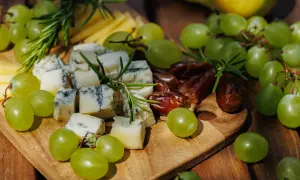 Un tagliere di legno con formaggio erborinato, uva verde succosa, datteri e rosmarino. Un perfetto abbinamento uva e formaggio per un aperitivo.