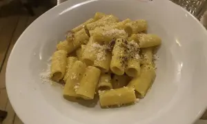 Piatto di rigatoni alla carbonara, conditi con guanciale croccante, pecorino romano e pepe nero. Perfetto con un bicchiere di vino bianco secco.