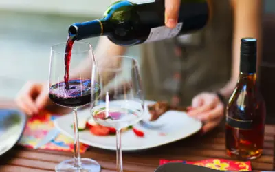 Versando vino rosso in un bicchiere, pronto per un perfetto abbinamento cibo vino con un piatto di carne e verdure.