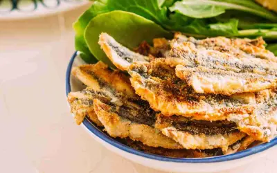 Piatto di alici fritte dorate e croccanti, servite con foglie verdi fresche.