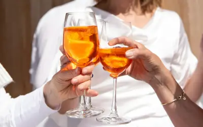 Tre mani brindano con bicchieri di Spritz arancione, un momento di gioia e leggerezza, pensando alle calorie spritz.