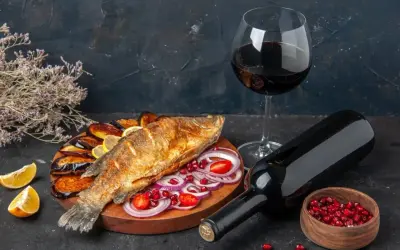 Un gustoso pesce fritto con melanzane, limone e cipolla, accompagnato da un bicchiere e una bottiglia di vino rosso da abbinare al pesce.