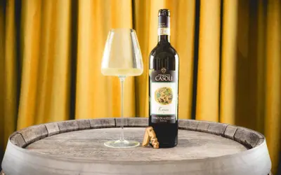 Un bicchiere di Fiano di Avellino DOCG e una bottiglia di vino Fiano di Avellino, su un vecchio barile di legno, con uno sfondo di tende dorate.