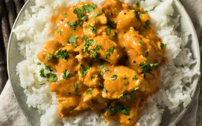 Piatto di riso bianco con pollo al curry arancione, guarnito con prezzemolo fresco. Perfetto con vino bianco o rosso.