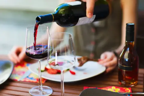 Versando vino rosso in un bicchiere, pronto per un perfetto abbinamento cibo vino con un piatto di carne e verdure.