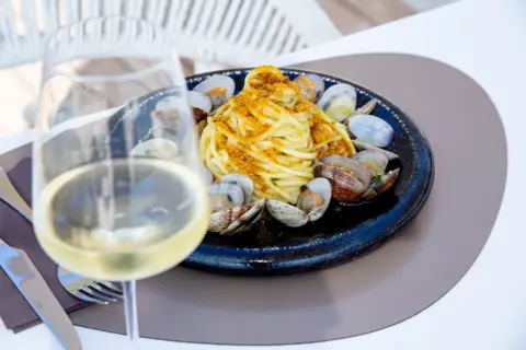 Un bicchiere di vino bianco, perfetto vino bianco da abbinare al pesce, accanto a un piatto di spaghetti alle vongole.