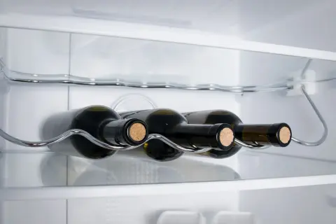Bottiglie di vino bianco su un ripiano cromato all'interno di un frigorifero.