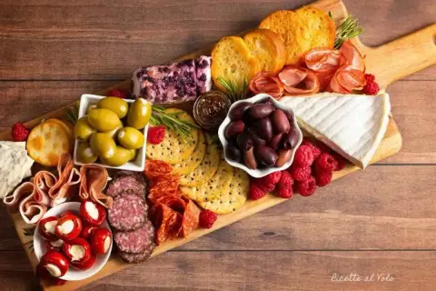 Un invitante tagliere di formaggi misti, salumi, olive, lamponi e crostini, perfetto per un aperitivo.