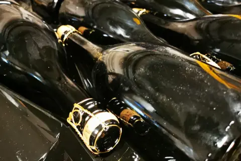 Bottiglie di vino scuro, pronte per la sboccatura. Le gabbie dorate promettono bollicine.