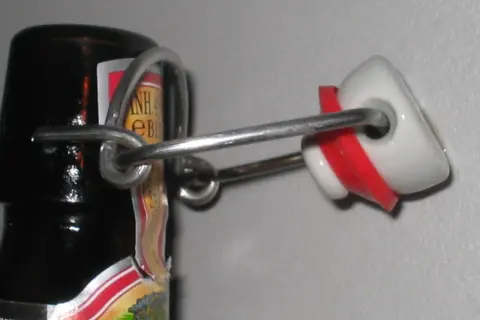 La bottiglia che si stappa da sola, con il suo tappo a scatto in ceramica bianca e rossa, evoca un senso di attesa e liberazione.