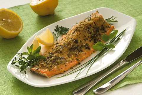 Filetto di trota salmonata cotto al forno con erbe aromatiche e limone, servito su un piatto bianco con guarnizioni fresche.