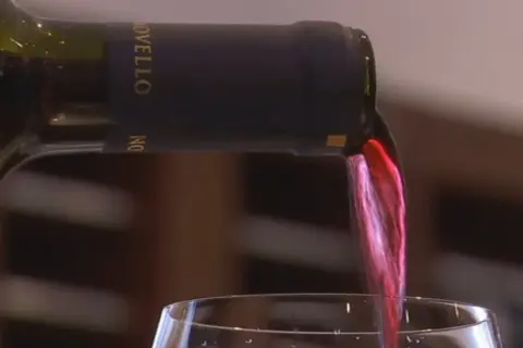 Versando vino rosso da una bottiglia con tappo a vite. Il liquido scorre nel bicchiere, creando un'onda cremisi.