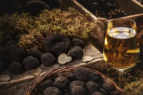 Truffles in a basket and on a wooden board, with a glass of white wine. La domanda è: che vino abbinare al tartufo?